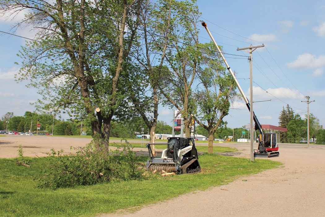 A telescoping boom allows a cutting tool to negotiate a series of power lines, while a skid steer handles the dropped-down material.